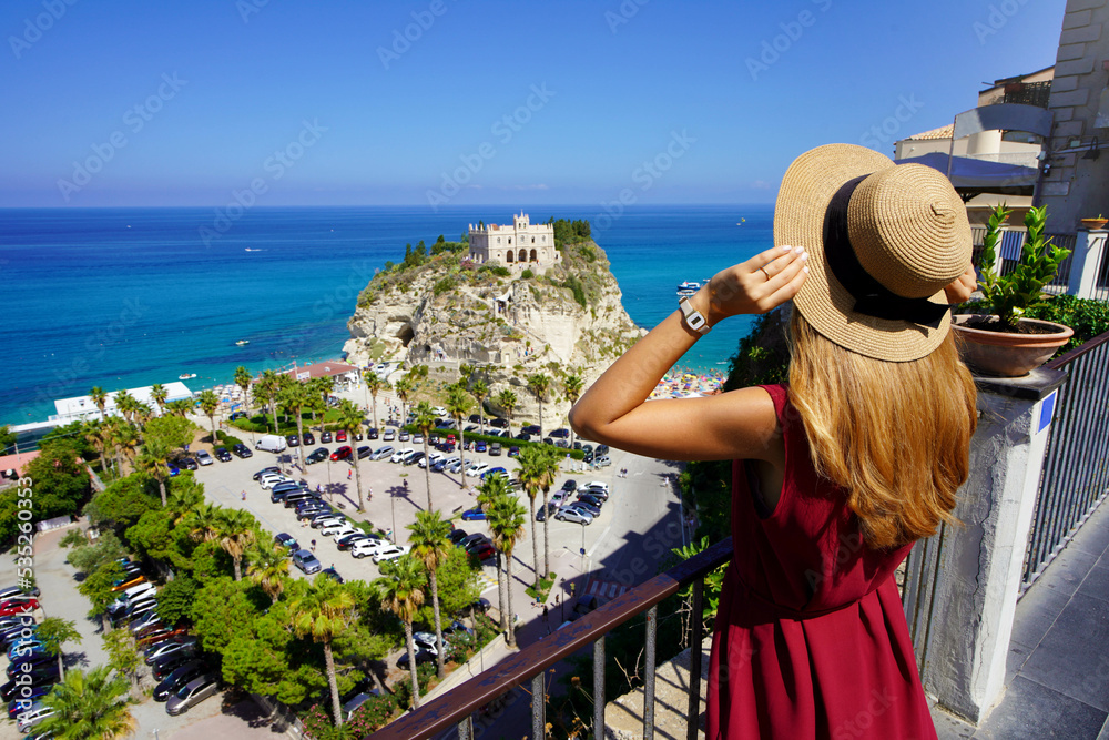 Holidays in Calabria. Back view of beautiful fashion girl enjoying view of Tropea village on Coast of the Gods, Calabria. Summer vacation in Italy.