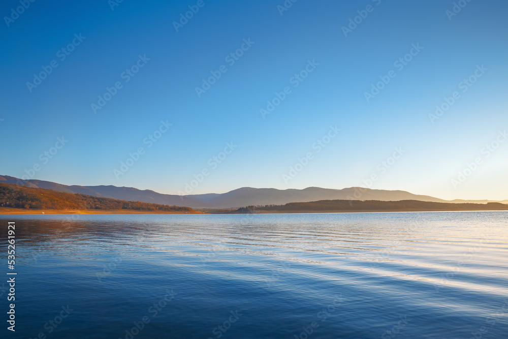 Beautiful sunrise over lake scenery in blue and yellow colors. Clear blue sky over calm lake during fantastic morning dawn.