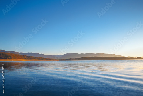 Beautiful sunrise over lake scenery in blue and yellow colors. Clear blue sky over calm lake during fantastic morning dawn.