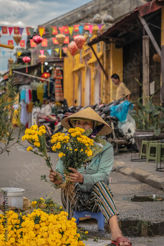 Vietnamese woman. Selling yellow flowers in the market. Peddling. Asian trip. Traditional market.