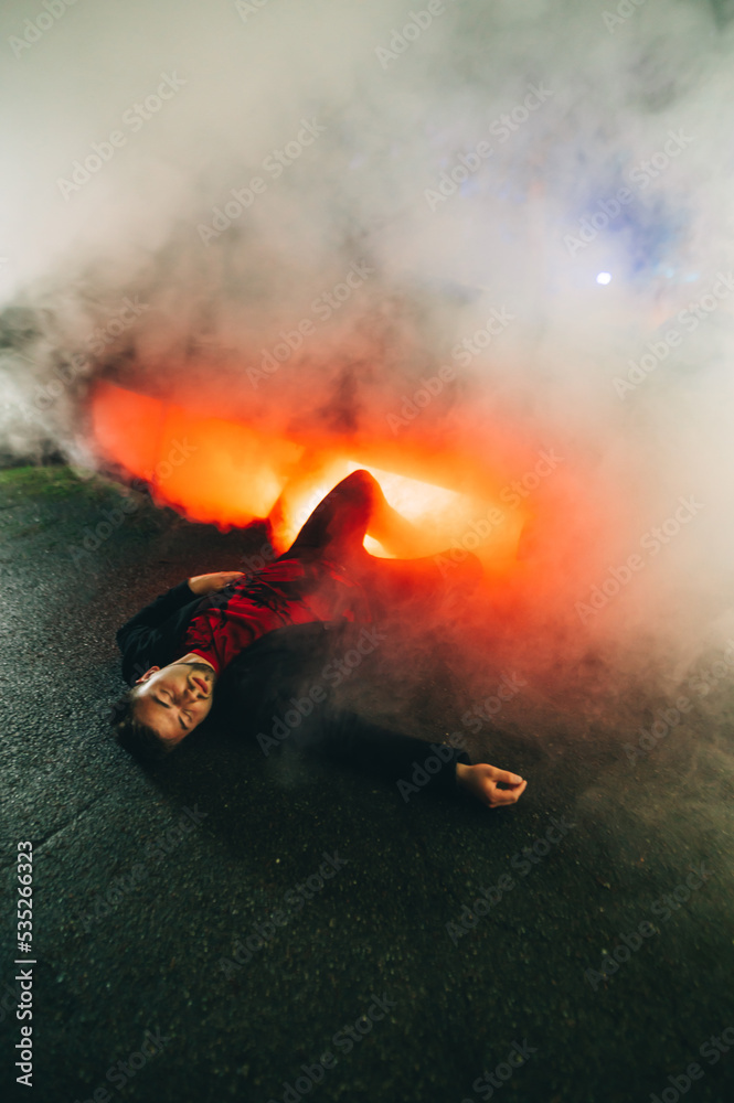 Obraz premium Adult man lying on the ground at night in the smoke near a burning car got into a car accident. Vertical