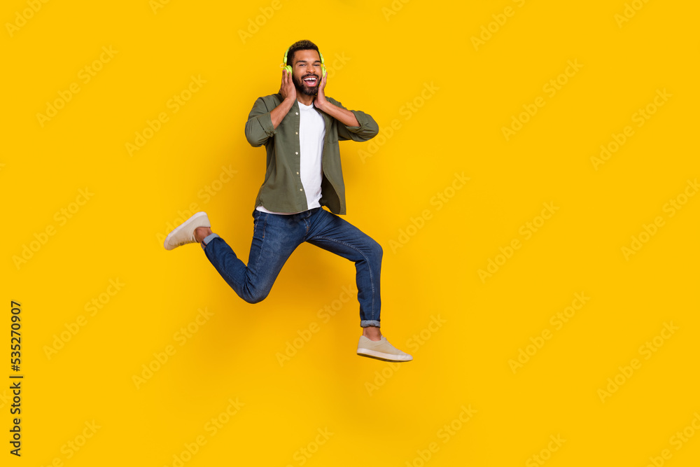 Full length photo of cheerful sweet man wear khaki shirt jumping high enjoying music empty space isolated yellow color background
