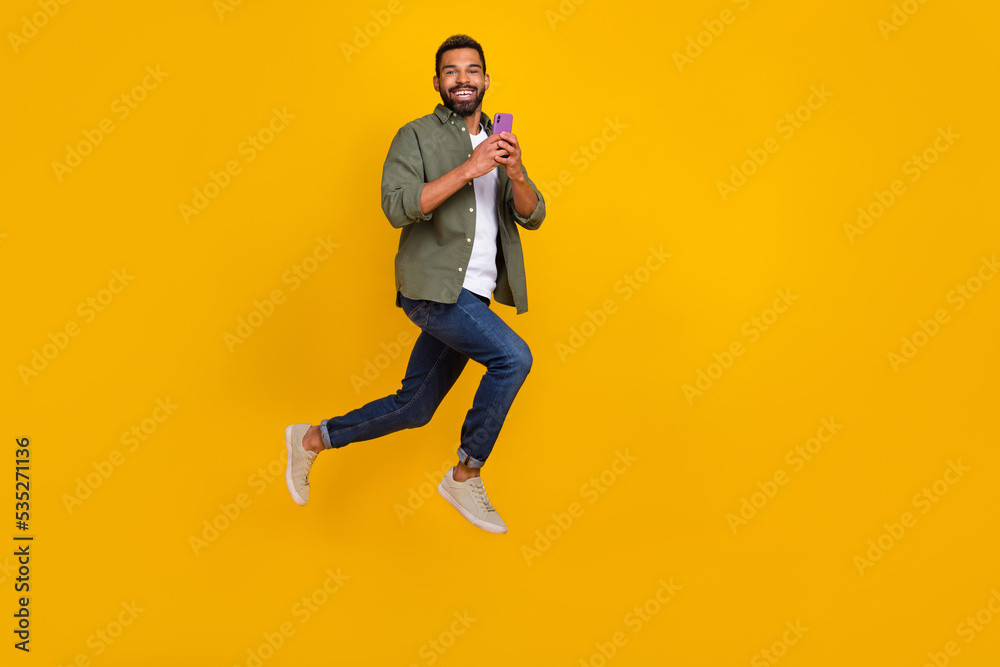 Full length photo of pretty cute man wear khaki shirt typing modern device empty space isolated yellow color background