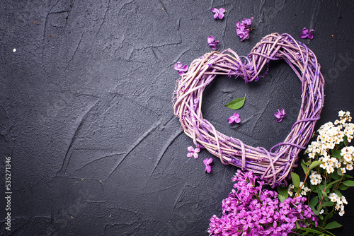 St. Valentine Day background greeting card. Decorative nandmade heart and lilac flowers on black textured background. Place for text. Top view. photo