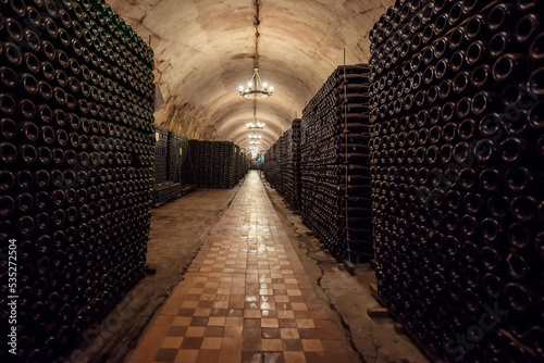 Glass wine bottles stacked in rows at winery storehouse. Wine-making produce storage at winery cellar. Wine cellar interior view. Wine making concept.