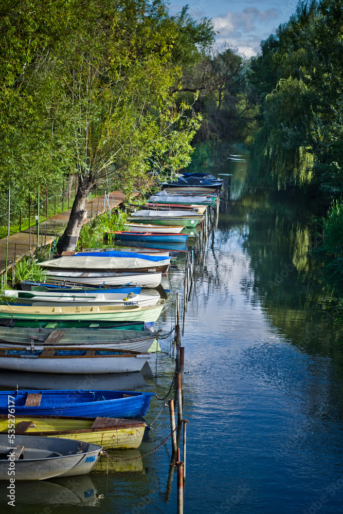 small colorful boats moored in a row at the pier in the river channel. in the background trees and plants