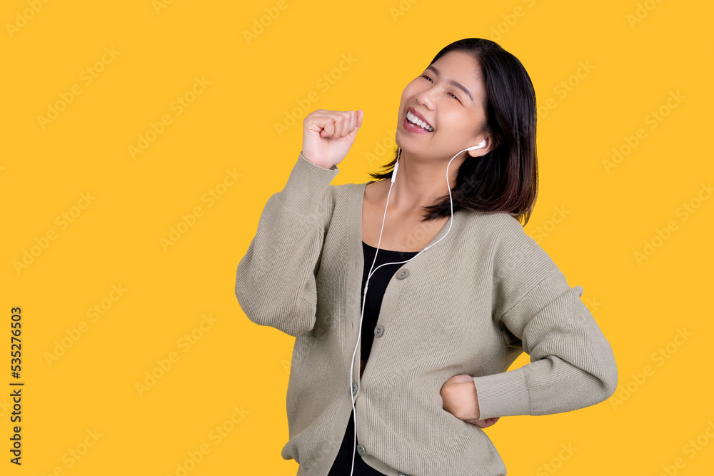 Happy Asian beautiful woman singing her favorite song. She is wearing white headphones isolated on a bright yellow background. Happy Asian beautiful woman singing her favorite song. She is wearing white headphones isolated on a bright yellow background.