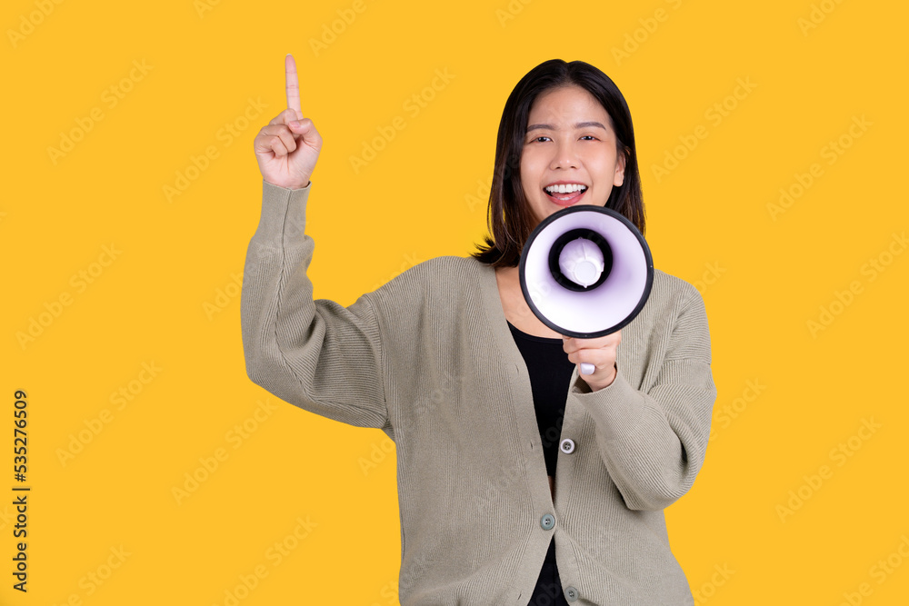 Happy Asian beautiful woman isolated on yellow background. She shouting through a megaphone and pointing side Happy Asian beautiful woman isolated on yellow background. She shouting through a megaphone and pointing side