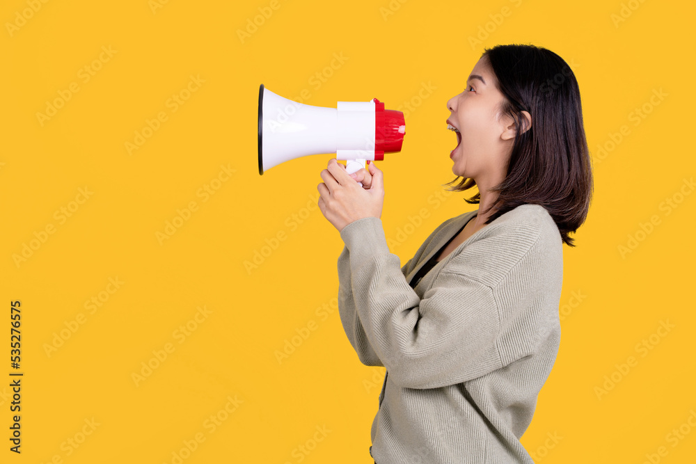 Beautiful Asian woman holding a megaphone and shouting out on a yellow background. She was excited in the side view. Beautiful Asian woman holding a megaphone and shouting out on a yellow background. She was excited in the side view.