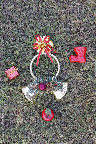 Decoraciòn para Navidad para colocar en la puerta con guirnalda redonda con campanillas, ramitas de pino, regalo y bota roja de Papà Noel, forma un alegre y original diseño con fondo del cèsped verde photo