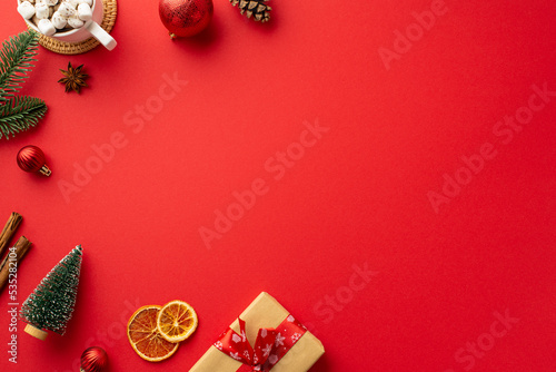 Christmas decorations concept. Top view photo of red baubles fir branch pine cones craft paper giftbox cup of cocoa and dried citrus slices on isolated red background with empty space © ActionGP