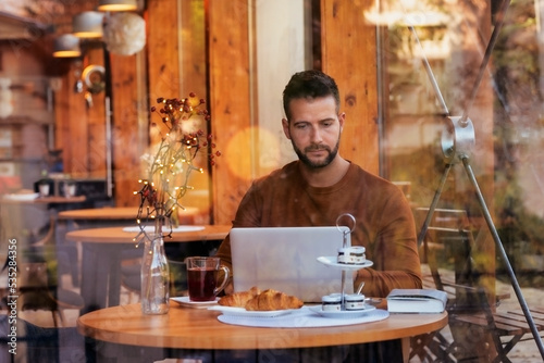 Man wearing casual clothes while sitting at table and using laptop in a cafe