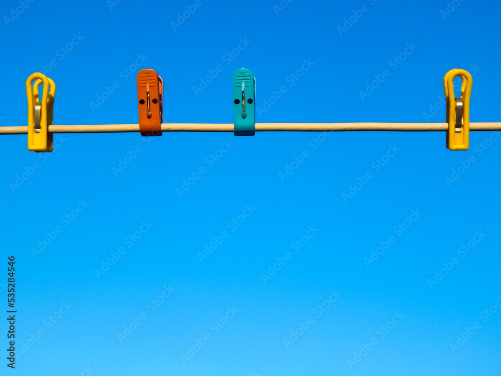 Clothespins of different colors attached to a drying rope against a blue sky