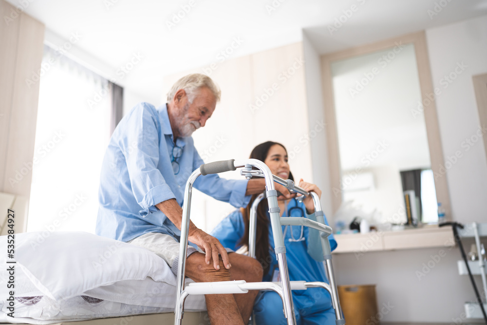 Obraz premium Portrait of Asian young nurse helping old elderly disable man grandfather to walk by using walker equipment in the bedroom. Senior patient of nursing home moving with walking frame and nurse support