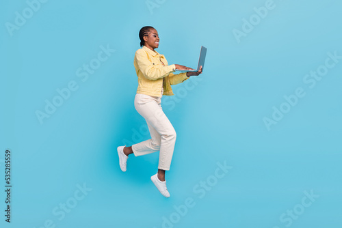 Full length body size view of beautiful trendy girl jumping using laptop writing email isolated on bright blue color background