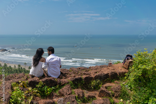 Beautiful young lovely attractive tourist couple looking each other, embracing, making love, smiling, cuddling enjoying sitting on the wall of Chapora fort, Goa. Dil Chahta Hai, beaches, horizon, love