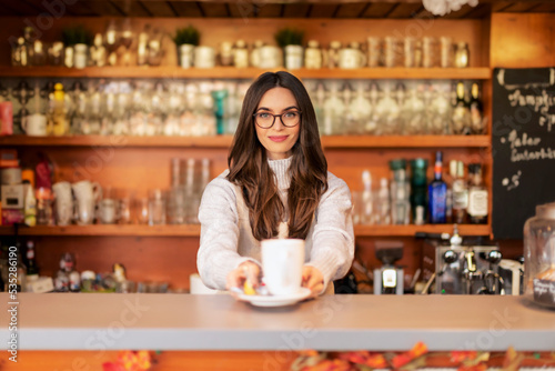 Shot of smiling waitress standing behind the counter and holding a cup of tea in her hand