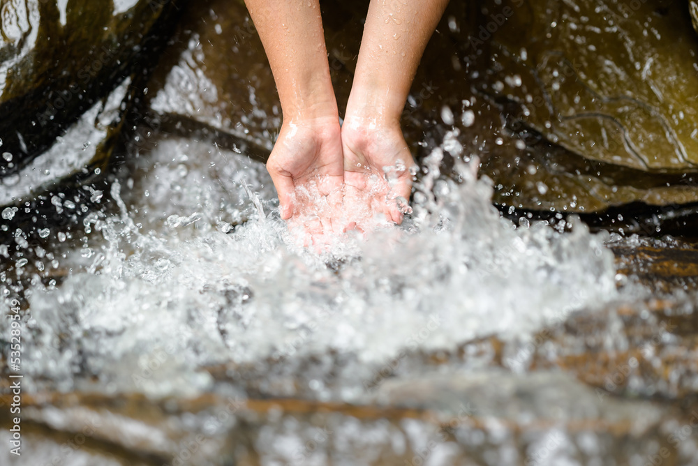 Closeup hands of a woman are outstrecthed and receiving the splash water from the stones in the creek while relaxing in the forest Closeup hands of a woman are outstrecthed and receiving the splash water from the stones in the creek while relaxing in the forest