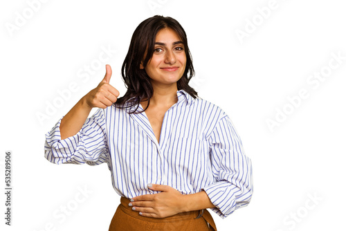 Young Indian woman isolated on green chroma background touches tummy, smiles gently, eating and satisfaction concept. photo