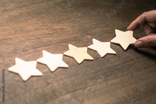 Hand fill the wooden star in a row on wood background, five stars rating, review, and feedback concept