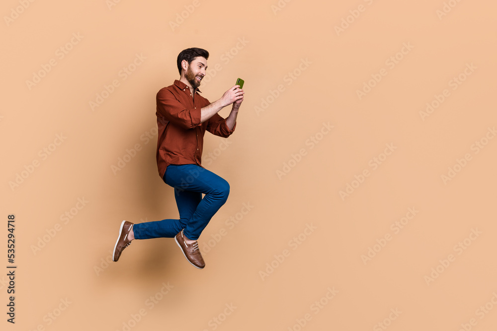 Full size profile portrait of handsome guy jump hold use telephone chatting isolated on beige color background Full size profile portrait of handsome guy jump hold use telephone chatting isolated on beige color background
