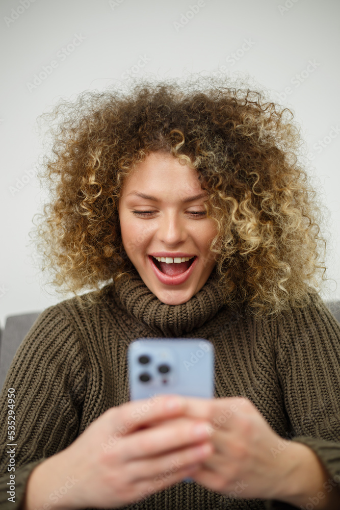 Excited young woman with smartphone. Portrait of happy white female reading a message on social media app in mobile phone Excited young woman with smartphone. Portrait of happy white female reading a message on social media app in mobile phone