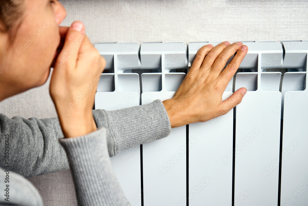 Woman warming her hands on the heater, close-up