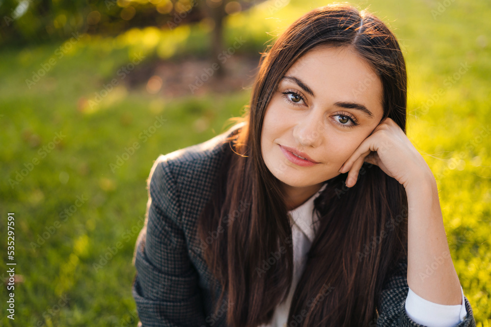 Portrait of young caucasian businesswoman with long hair enjoying coffee break on green grass, copy space in city park. Happy female outdoor working with