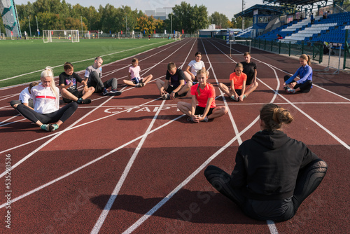 Fototapeta Naklejka Na Ścianę i Meble -  Female coach and group of children conducts a training session at the stadium. School gym trainings or athletics