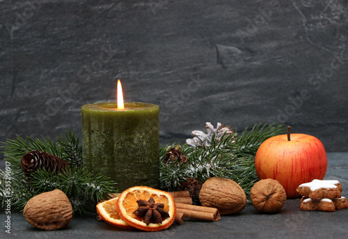 Christmas arrangement with green candle, nuts, apple, cinnamon and fir branches