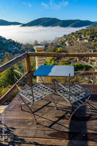 View of two metal traditional chairs with a table in Ano Pedina village a misty autumn morning with its architectural traditional old stone buildings located on Tymfi mount, Zagori, Epirus, Greece.