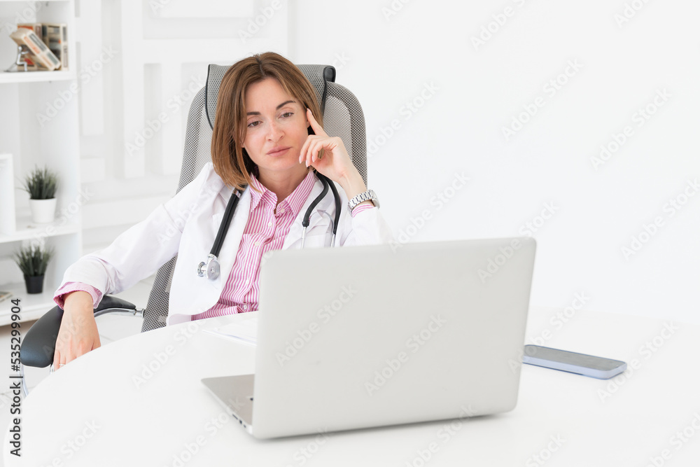 Young attractive female doctor sitting at the desktop in the office and consulting her patient online Young attractive female doctor sitting at the desktop in the office and consulting her patient online