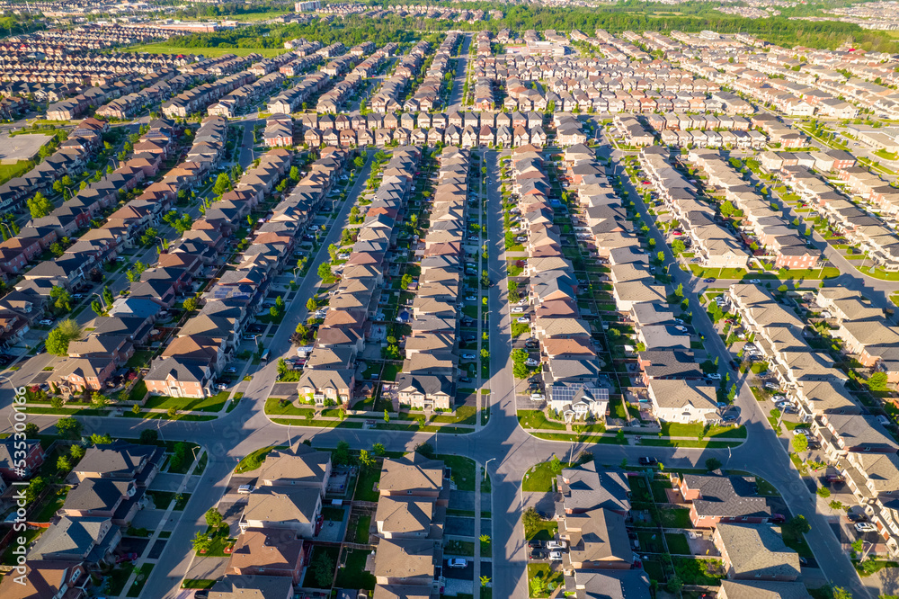 Aerial footage of Canadian town showing suburban housing estates in geometrical position and rows of houses. Summer golden hour evening with long shadows.