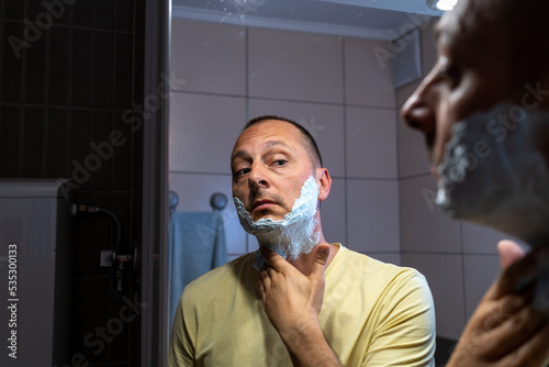 Mature handsome man shaving in front of mirror