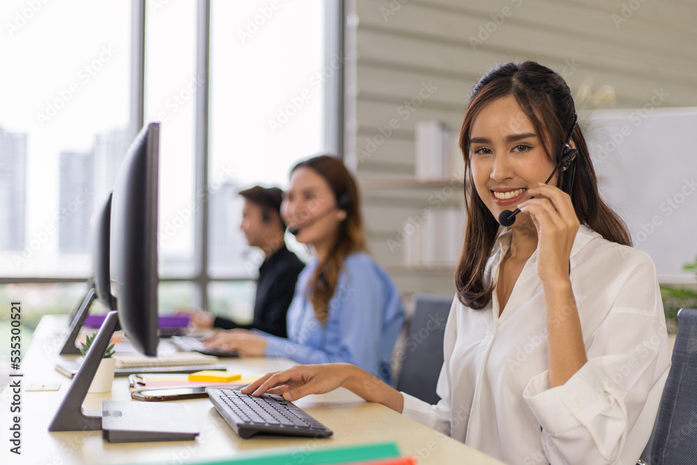 Smiling asian call center agent with headset working on support in the office. Smiling asian call center agent with headset working on support in the office.