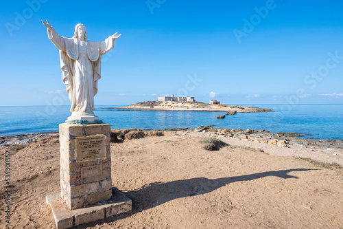 The statue of Christ Redeemer in Portopalo with the Island of Correnti in background photo