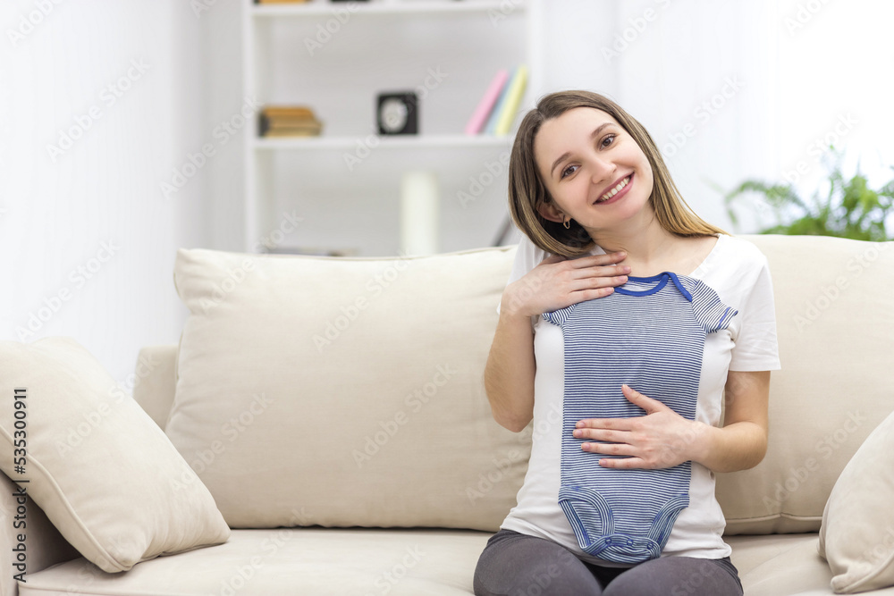 Photo of pregnant woman wearing casual clothes and holding childish clothes in hands. Photo of pregnant woman wearing casual clothes and holding childish clothes in hands.