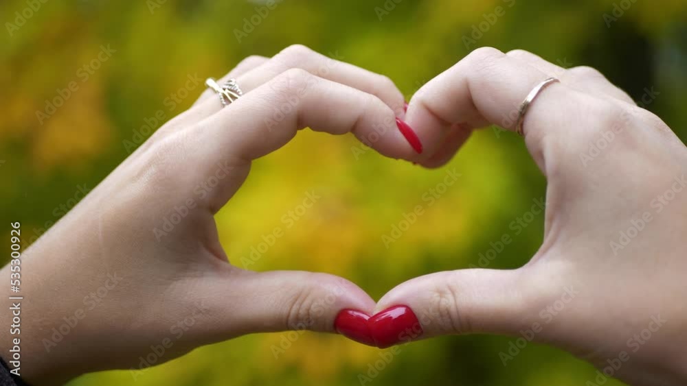 A girl with red manicure fingers shows a heart on a blurry autumn background. Like, approval, expression of sympathy. A girl with red manicure fingers shows a heart on a blurry autumn background. Like, approval, expression of sympathy.