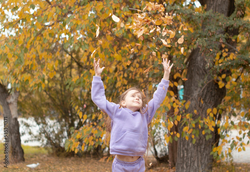 charming happy girl throws up fallen leaves while playing in an autumn park and laughs on a sunny day Feeling inner peace, happiness, harmony. Selective focus