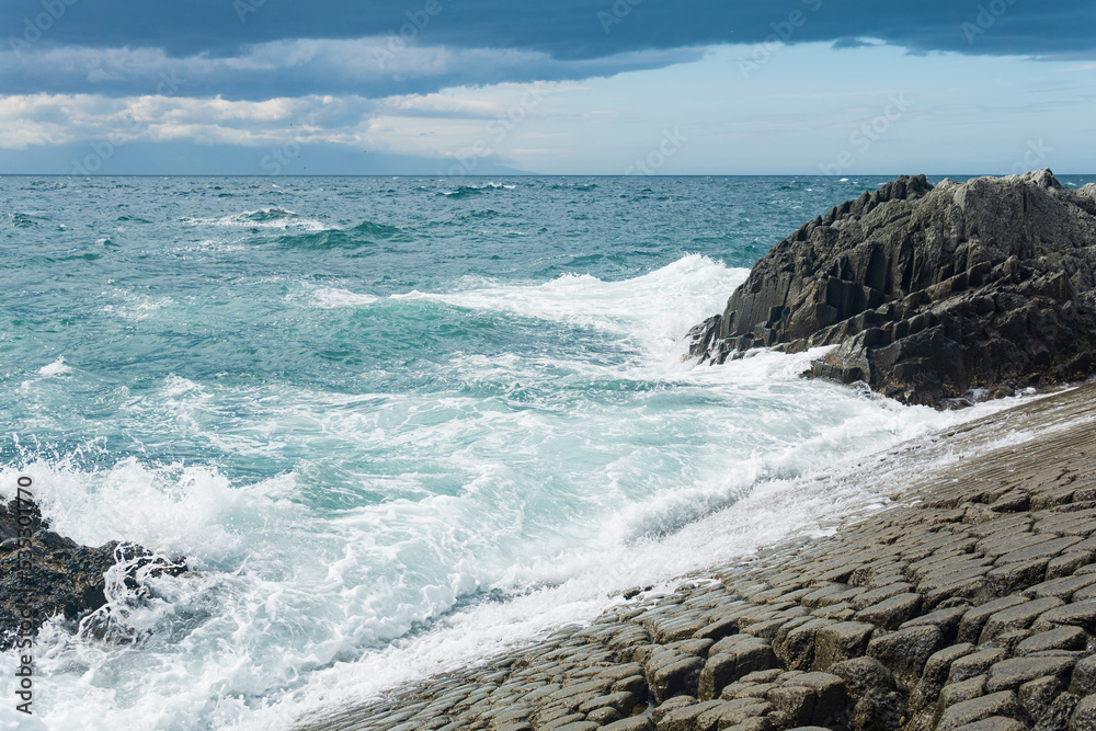 rocky seashore formed by columnar basalt against the surf, coastal landscape of the Kuril Islands