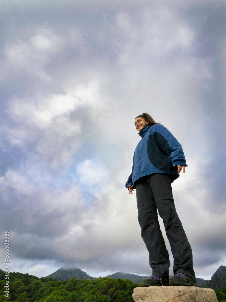 Girl on top of a rock looks at the horizon smiling under a cloudy sky. Girl on top of a rock looks at the horizon smiling under a cloudy sky.