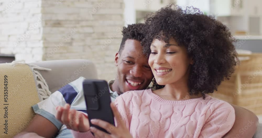 Happy african american couple using smartphone together in living room Happy african american couple using smartphone together in living room