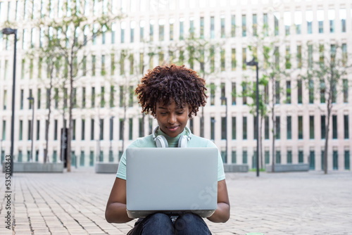 Young student sitting on the stairs outdoors and typing on her laptop