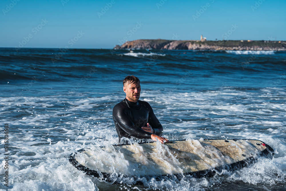 Man holding his surfboard on the shore, while fighting against the current of the sea.