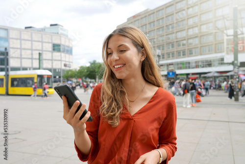 Smiling woman using smartphone in Alexanderplatz square in Berlin, Germany