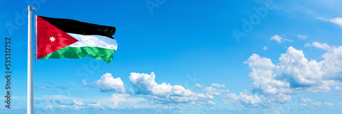 Jordan flag waving on a blue sky in beautiful clouds - Horizontal banner photo