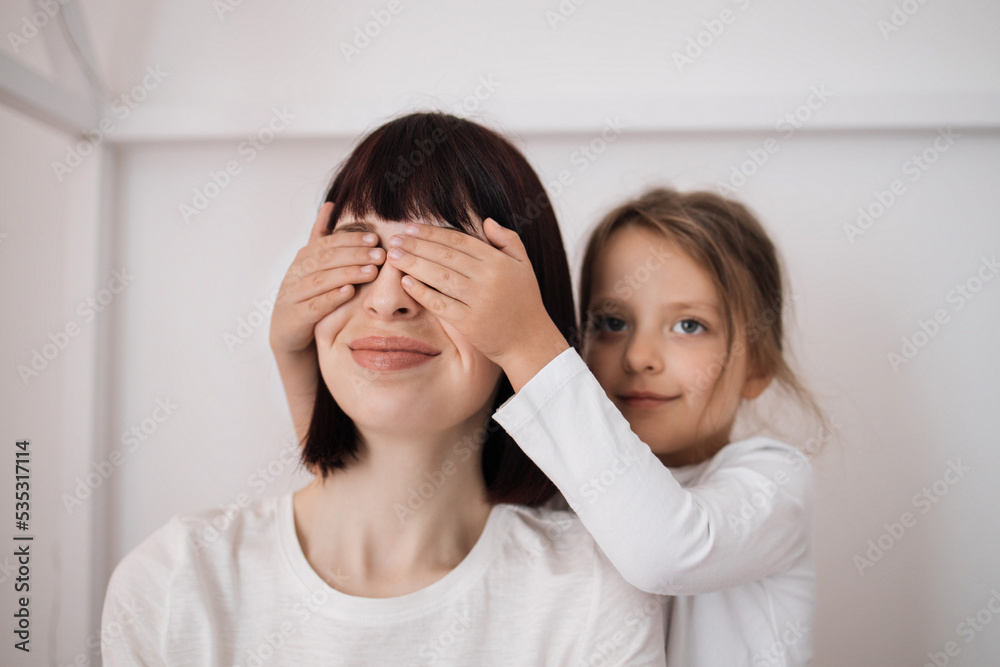 Satisfied caucasian preschooler girl closes eyes to young lady and congratulates with birthday, sitting on bed in bedroom interior. Surprise, holiday, love and relationship. Celebrate at home Satisfied caucasian preschooler girl closes eyes to young lady and congratulates with birthday, sitting on bed in bedroom interior. Surprise, holiday, love and relationship. Celebrate at home