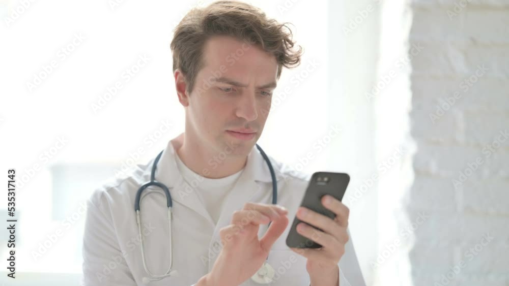 Young Doctor using Smartphone While sitting in Clinic Young Doctor using Smartphone While sitting in Clinic