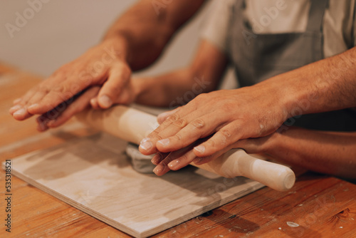 Male and female hands work in a pottery workshop. Roll out the ceramics with a rolling pin.