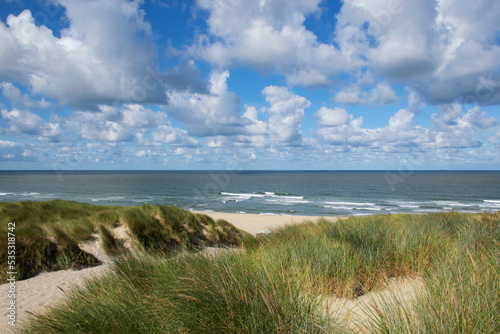 high view point on top of large sand dune looking towards the beach and the sea. Grasses on top of dunes. blue sky and white clouds. Summer landscape at the texel in the netherlands. Dutch seascape photo